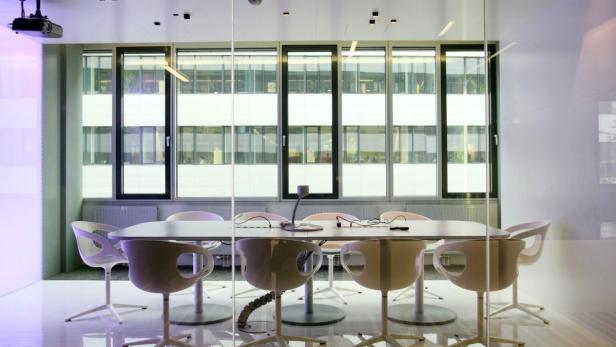 Ein Konferenzraum mit einem langen Tisch und modernen Stühlen vor einer Fensterfront.