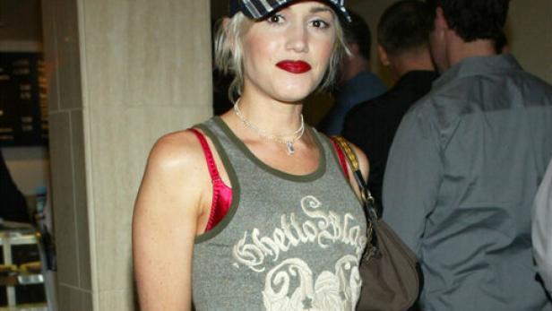 Gwen Stefani trägt ein Tanktop, Baggy Jeans, rote Schuhe und eine Kappe.