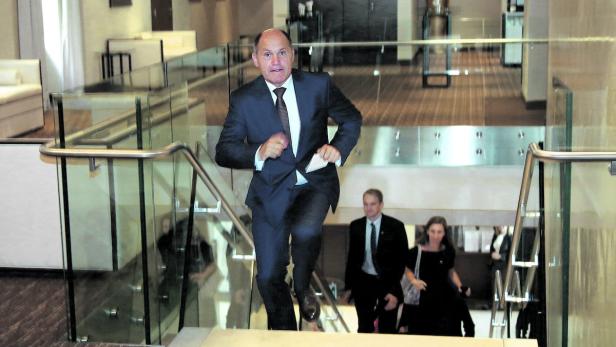 Ein Mann in einem Anzug eilt eine Treppe hinauf, gefolgt von zwei weiteren Personen.