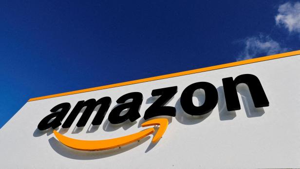 Das Amazon-Logo mit gelbem Pfeil ist auf einer weißen Wand vor blauem Himmel zu sehen.