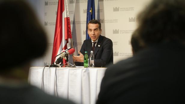 Ein Mann in Anzug spricht bei einer Pressekonferenz vor Flaggen.