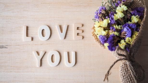 Ein Blumenstrauß liegt neben den hölzernen Buchstaben „Love You“.