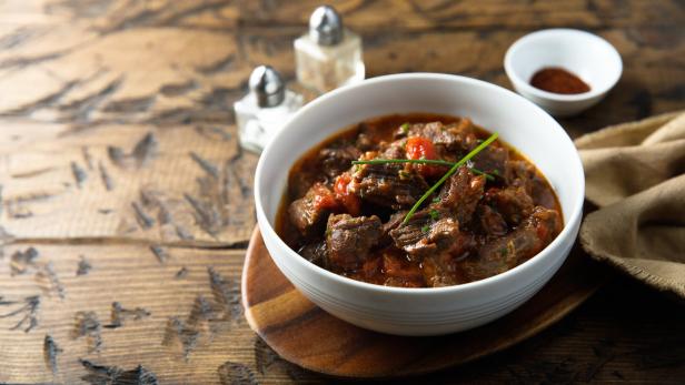 Rindfleischgulasch in einer Schüssel auf einem Holztisch.