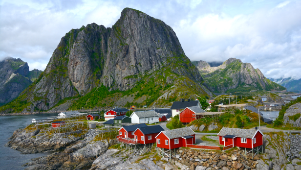Rote Holzhäuser in einem Fischerdorf vor einer beeindruckenden Bergkulisse in Norwegen.