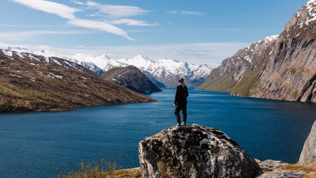 Eine Person steht auf einem Felsen und blickt auf einen See und schneebedeckte Berge.