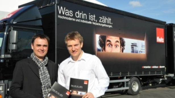 Zwei Männer stehen vor einem LKW mit der Aufschrift „Was drin ist, zählt“.