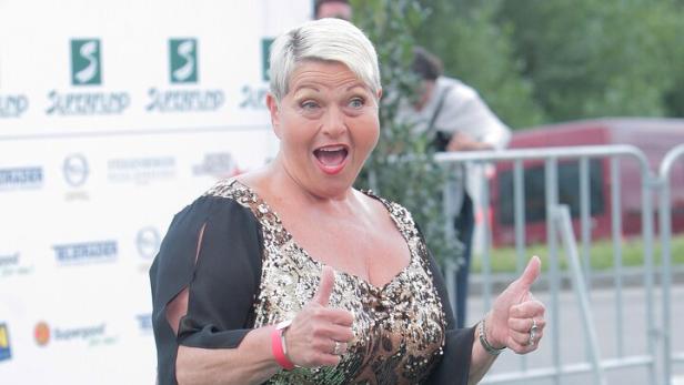 Eine Frau im goldenen Paillettenkleid gibt zwei Daumen hoch.