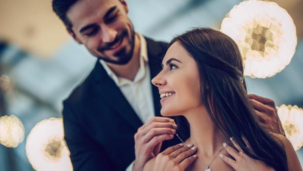 Ein Mann schenkt einer Frau eine Halskette und legt sie ihr um den Hals.