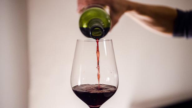 Person schenkt Rotwein aus Flasche in Glas ein