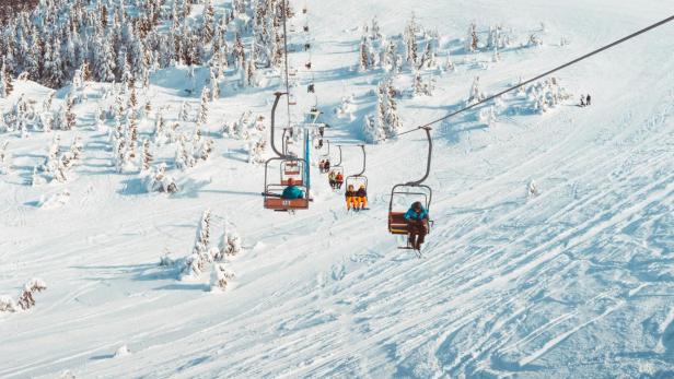 Skifahrer werden mit einem Sessellift auf einen schneebedeckten Berg befördert.