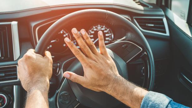 Eine Person betätigt die Hupe in einem Auto.
