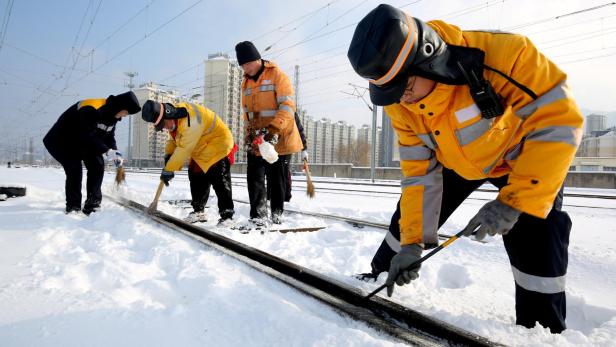 Chinesische Arbeiter räumen Gleise vor dem Bahnhof Lianyungang East von Schnee und Eis frei