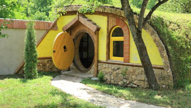 Ein gelbes Hobbit-Haus mit runder Tür und Fenster in einem grünen Hügel.