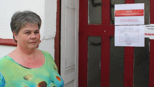 Eine Frau steht vor einer Tür mit einem Schild „Kein Wohnungsverkauf!“.