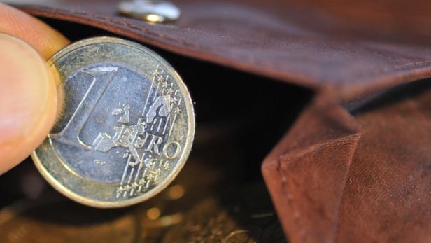 Eine Hand legt eine 1-Euro-Münze in ein braunes Lederportemonnaie.