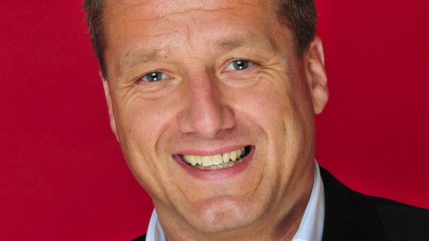 Ein lächelnder Mann vor einem roten Hintergrund.