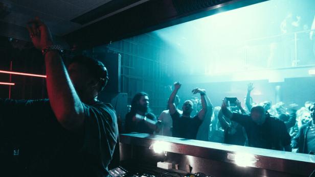 Ein DJ legt in einem Club vor einer jubelnden Menge auf.