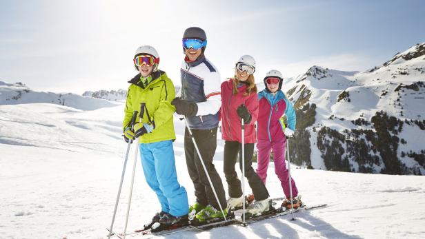 Eine Familie steht auf Skiern vor einer verschneiten Berglandschaft.