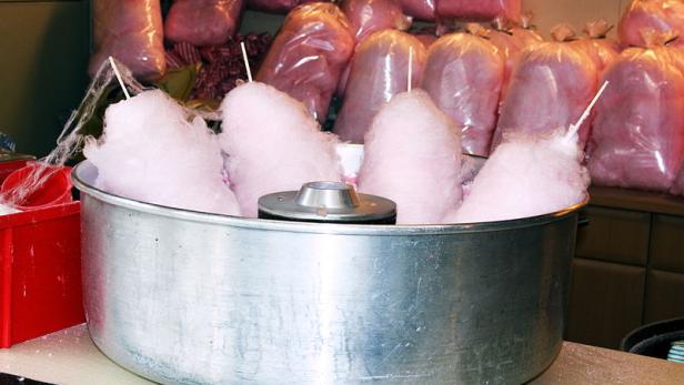 Zuckerwatte wird in einer Maschine zubereitet, im Hintergrund abgepackte Portionen.