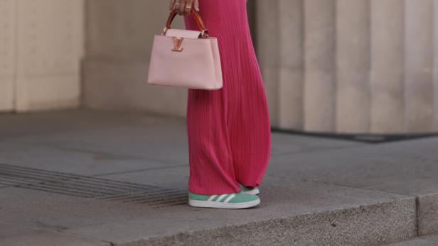 Eine Frau in einem pinkfarbenen Kleid mit einer hellrosa Louis Vuitton Handtasche und grünen Adidas-Sneakers.