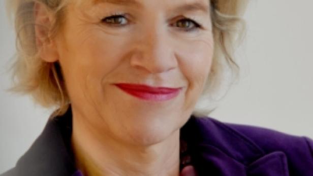 Eine Frau mit blonden Haaren und einer lila Jacke lächelt.