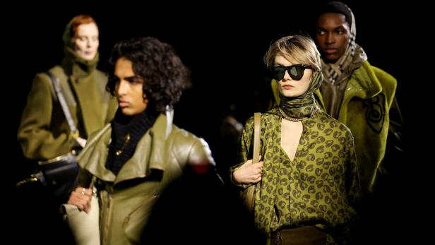 Mehrere Models präsentieren grüne und braune Kleidung auf einem Laufsteg.