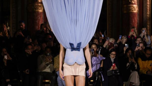 Ein Model mit einem großen, hellblauen Tüll-Hut auf dem Laufsteg.