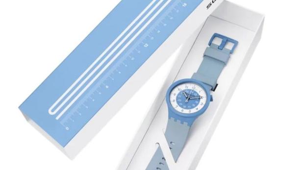 Eine hellblaue Swatch-Uhr liegt in einer weißen Schachtel, deren Deckel daneben liegt.