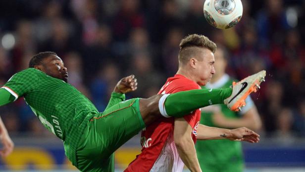 Ein Fußballspieler in Grün tritt nach dem Ball, während ein Gegenspieler in Rot daneben steht.