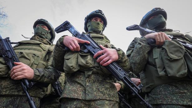 Drei Soldaten in Tarnuniformen stehen mit Gewehren da.