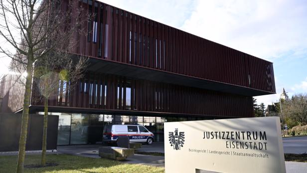 Modernes Justizzentrum mit brauner Fassade, davor ein Polizeiauto und ein Schild mit der Aufschrift „Justizzentrum Eisenstadt“.