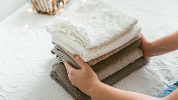 Ein Stapel gefalteter Textilien in neutralen Farben wird von Händen gehalten.