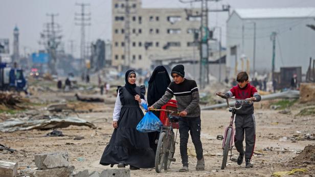 Teenager spazieren mit Rädern durch kaputte Straße im Gazastreifen.