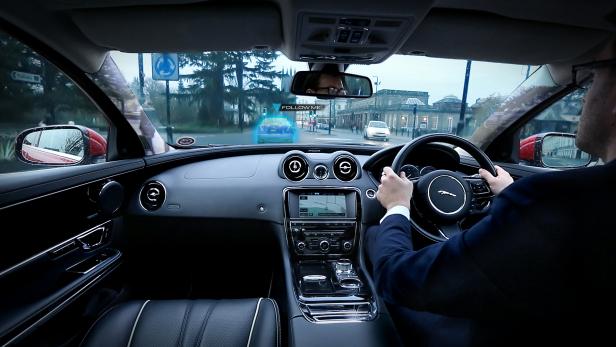 Ein Mann fährt einen Jaguar mit Head-up-Display, das ein vorausfahrendes Auto hervorhebt.