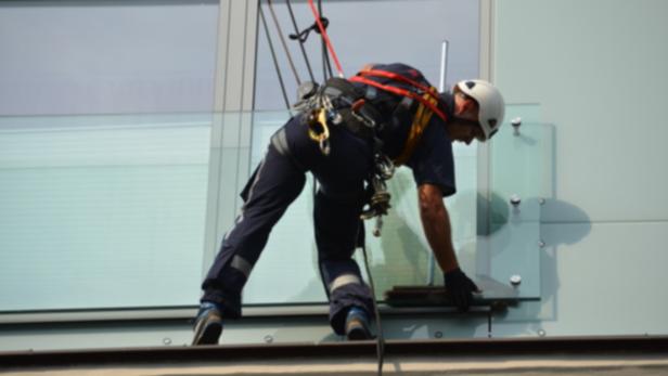 Ein Fensterputzer arbeitet an der Fassade eines hohen Gebäudes.