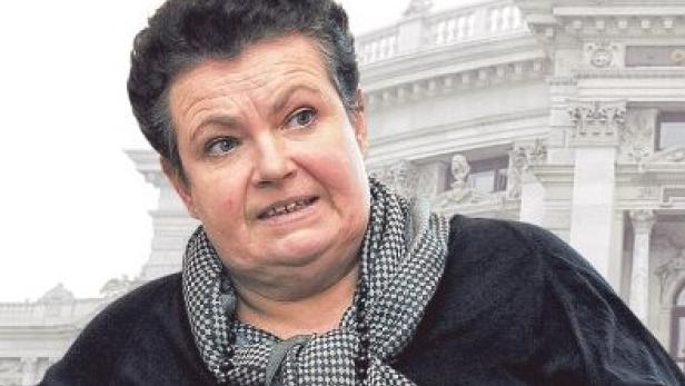 Eine Frau mit dunklem Haar und einem schwarz-weiß karierten Schal vor einem Gebäude.