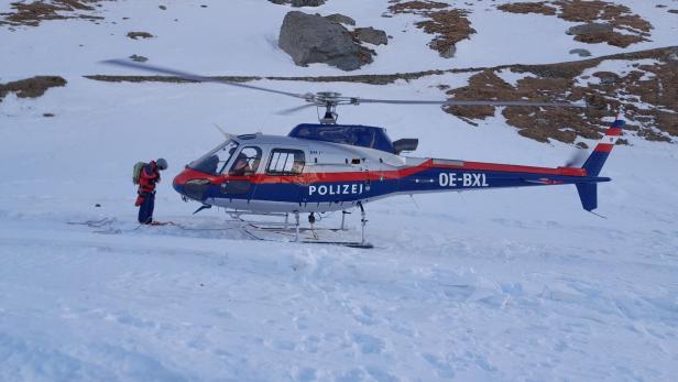 Ein Mann steht neben einem Polizei-Hubschrauber in einer verschneiten Berglandschaft.