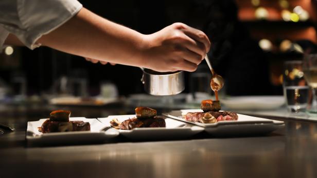 Ein Koch beträufelt Fleisch mit einer Soße.