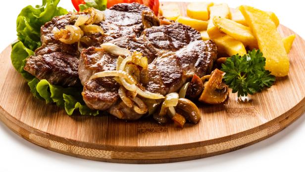 Ein Teller mit Steak, Zwiebeln, Pommes und Salat auf einem Holzbrett.