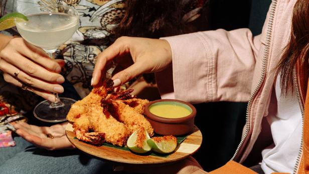 Personen teilen sich panierte Garnelen mit Limetten und einem Dip, dazu ein Cocktail.
