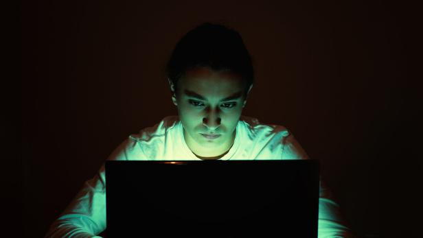 Ein Teenager sitzt in einem dunklen Raum vor dem Laptop.