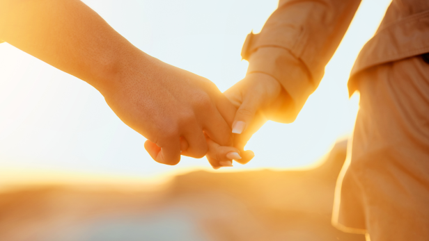 Ein Paar hält Händchen im goldenen Licht der Abendsonne.