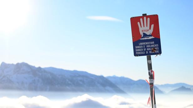 Ein Lawinengefahr-Schild steht vor einer verschneiten Berglandschaft.