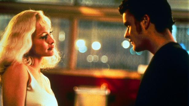 Eine blonde Frau und ein Mann stehen einander gegenüber.