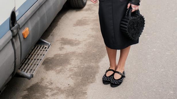 Eine Frau in schwarzer Lederjacke und Rock steht neben einem Polizeiwagen.