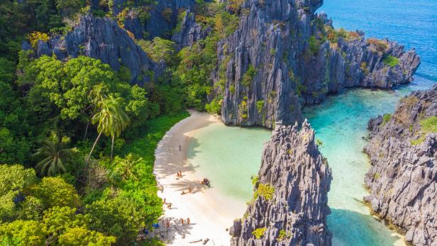 Luftaufnahme einer malerischen Bucht mit türkisfarbenem Wasser, weißem Sandstrand und üppiger Vegetation.