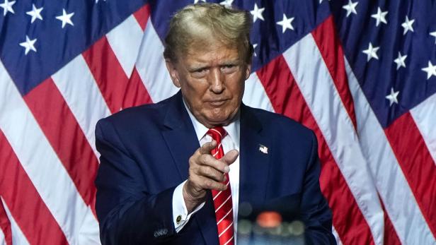 Donald Trump vor US-Flaggen deutet mit Finger auf den Fotografierenden