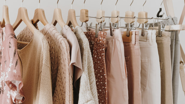 Eine Kleiderstange mit verschiedenen Kleidungsstücken in Rosa-, Beige- und Grautönen.