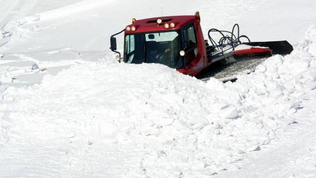 Eine rote Pistenraupe schiebt eine große Menge Schnee vor sich her.