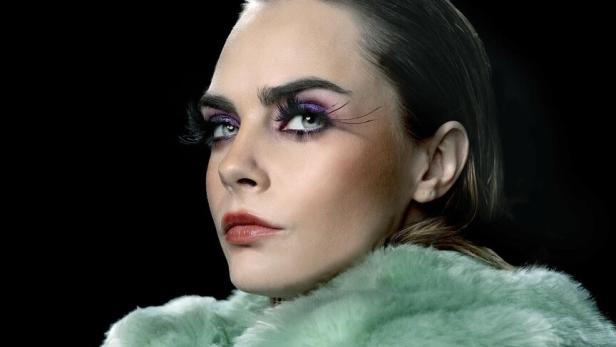 Cara Delevingne trägt einen mintgrünen Pelzmantel und auffälliges Augen-Make-up.